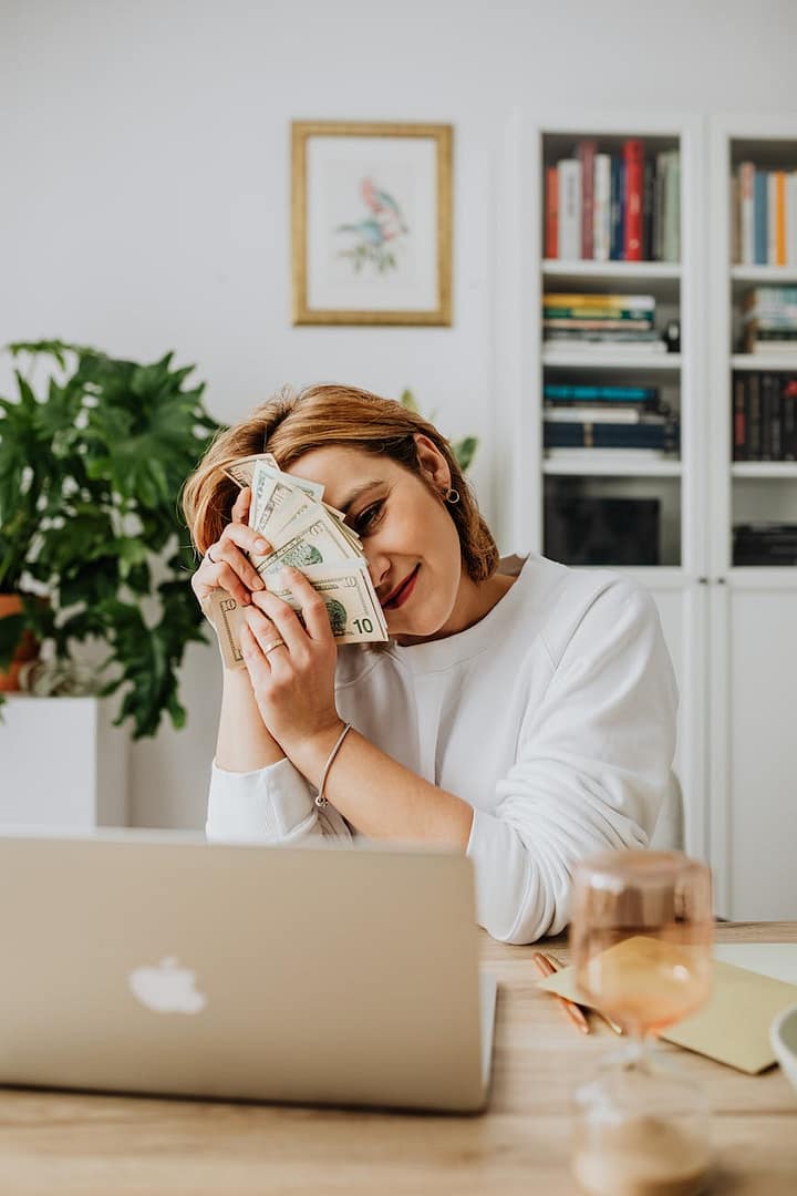 woman sitting in front of her laptop and holding a lot of cash